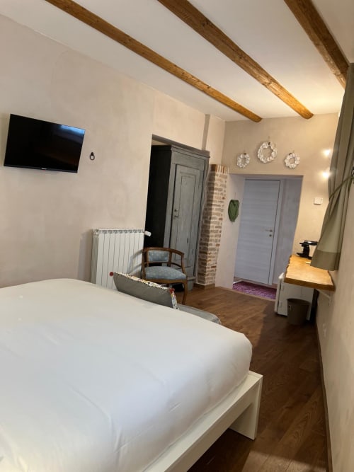 Spacious Iris Double Room at La Cascina di Bea with white bed, exposed wooden beams, flat-screen TV, and modern amenities in
