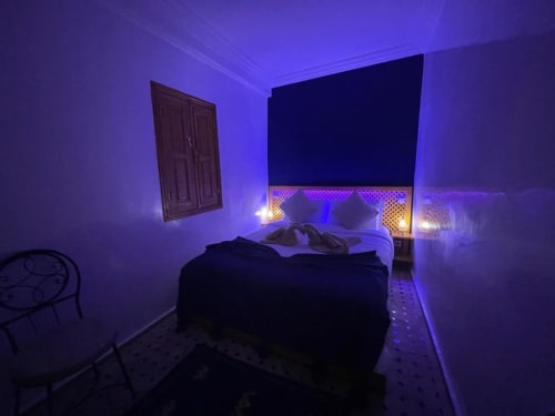 Chambre illuminée de violet au Riad Madinina à Marrakech avec lit, éclairage ambiant et porte traditionnelle en bois