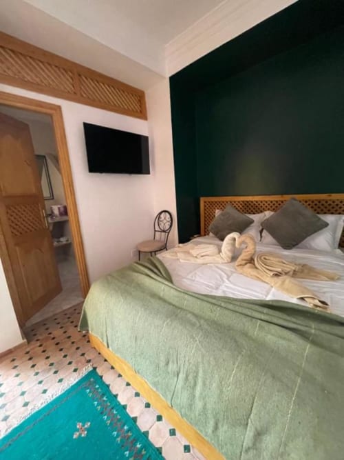 Chambre moderne au Riad Madinina à Marrakech avec mur d'accent vert, lit en bois et tapis turquoise