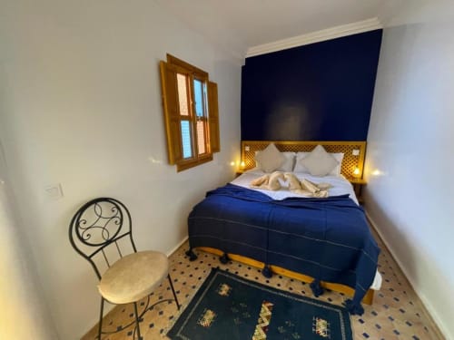 Riad Madinina bedroom in Marrakech with blue headboard, white pillows, decorative chair, and traditional zellige tile floor