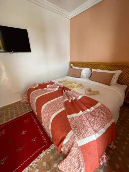 Chambre de riad à Marrakech avec lit queen-size, plaid rayé rouge, TV murale, murs blanc et pêche
