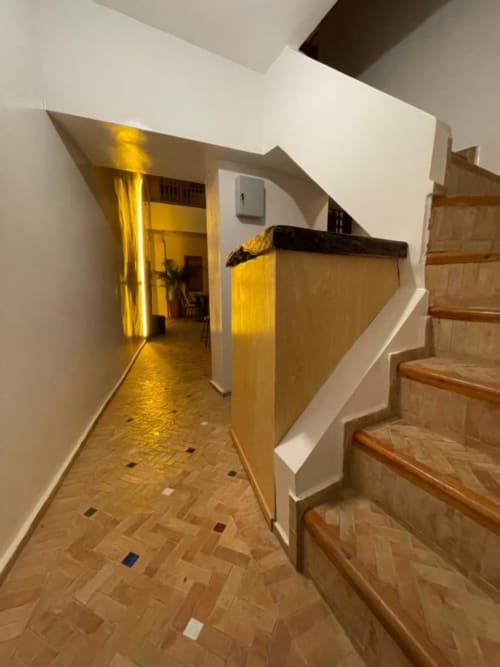Hallway at Riad Madinina in Marrakech with wooden stairs, white walls, and warm yellow lighting