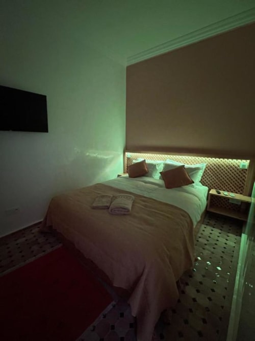 Chambre du Riad Madinina à Marrakech avec éclairage ambiant vert, lit moderne avec oreillers et table de nuit
