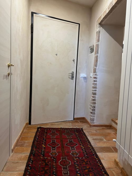 Entrance hallway at La Cascina di Bea B&B with red patterned rug, wooden flooring, and modern door with black frame