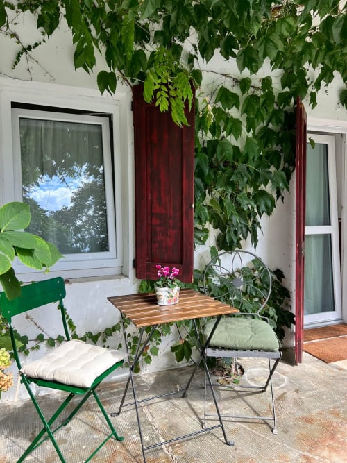 Cozy garden patio at La Cascina di Bea with green chair, wooden table, pink flowers, and ivy-covered white walls in Bergamo,