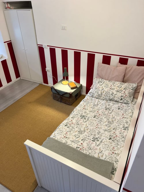Dalia room at La Cascina di Bea, Bergamo: single bed with floral bedding, red-striped headboard, wardrobe, and garden view.