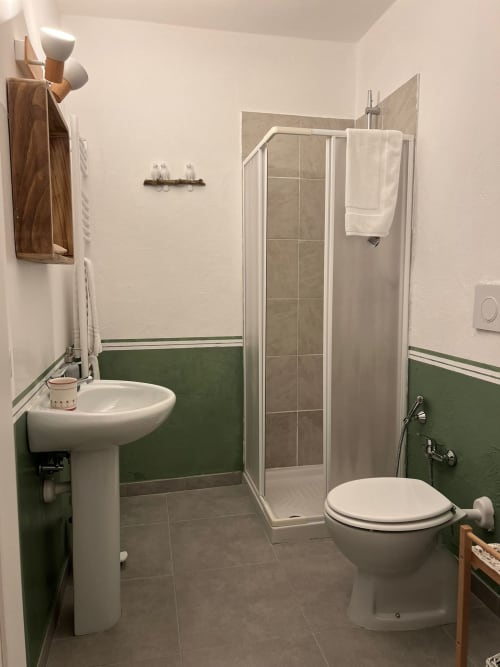 Modern bathroom at La Cascina di Bea in Bergamo with pedestal sink, toilet, and walk-in shower with green half-tile walls