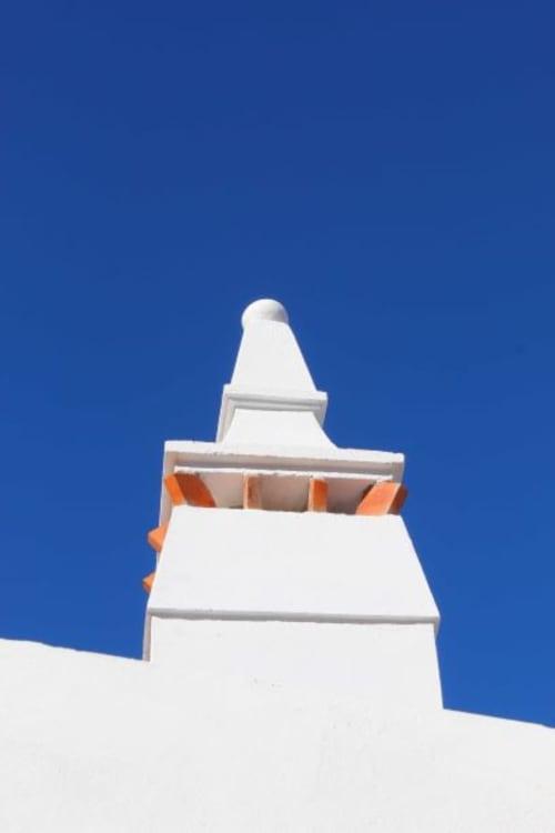 White chapel with orange accents against blue sky at Casas de Juromenha, Portugal