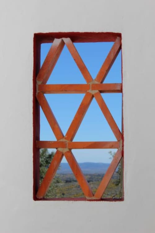 Rustic red wooden window with diagonal bracing framing scenic Alentejo landscape view at Casas de Juromenha
