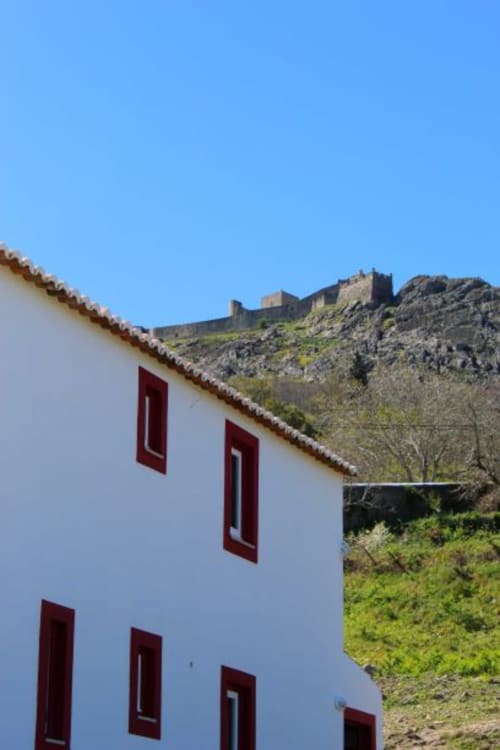 White building with red-framed windows at Casas de Juromenha, with historic castle ruins on hillside