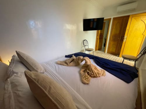 Chambre spacieuse du Riad Madinina à Marrakech avec literie blanche, TV murale et portes jaunes traditionnelles
