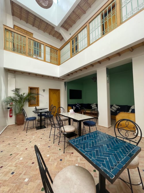 Salon de la cour du Riad Madinina à Marrakech avec tables de salle à manger, murs verts, balustrades en bois et architecture traditionnelle