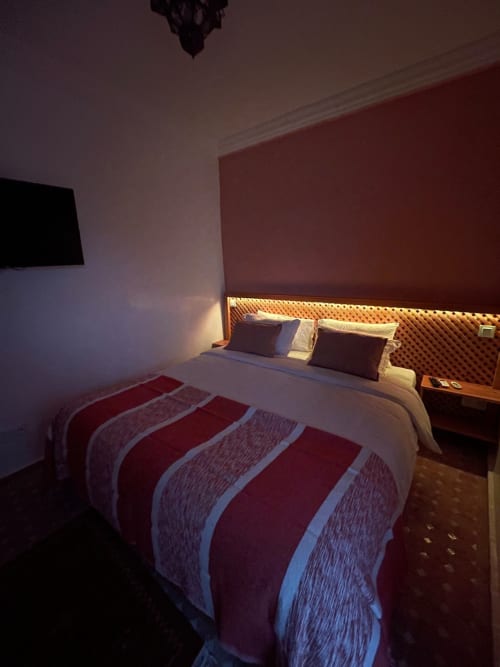Chambre du Riad Madinina à Marrakech avec literie rayée, éclairage ambiant de tête de lit et mur d'accent bordeaux