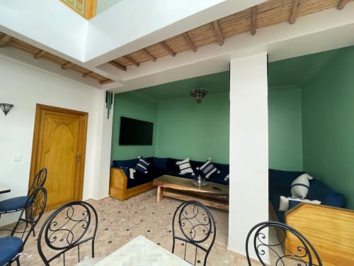 Cottage Riad Madinina à Marrakech : murs verts, poutres en bois, sièges bleus et décoration marocaine traditionnelle