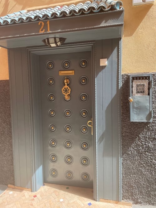 Porte grise ornementée avec quincaillerie dorée à l'entrée du Riad Madinina, boutique hôtel de Marrakech, présentant des motifs circulaires
