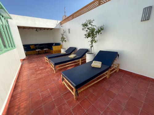 Terrasse sur le toit du Riad Madinina avec transats en bois, coussins bleu marine et plantes en pot à Marrakech
