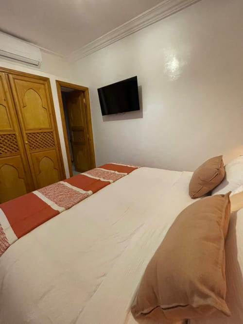 Chambre confortable au Riad Madinina à Marrakech avec literie blanche, coussins beige, portes en bois et TV murale