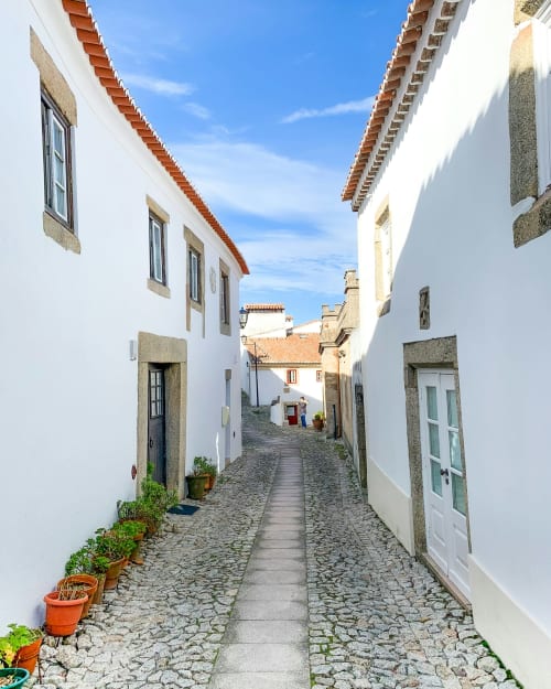 Charming cobblestone alley at Casas de Juromenha hotel in Portugal with whitewashed buildings and terracotta roofs under blue