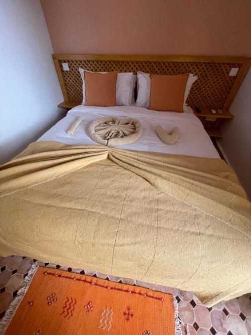 Marrakech riad bedroom with traditional decor, orange and beige pillows, towel art, and geometric rug.