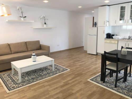 Apartamento open-plan em Sintra com sofá bege, mesa de centro branca, conjunto de jantar preto, cozinha creme com eletrodomésticos e acabamentos em madeira