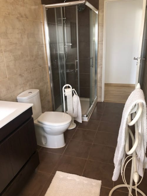 Banheiro moderno no Sintra Apartamentos com box, sanitário, pia e toalhas brancas nos toalheiros