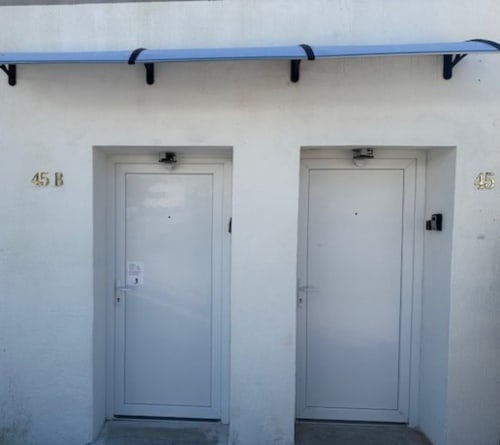 Vista exterior do Sintra Apartamentos com duas portas brancas numeradas 45B e 45, toldo azul e área privada