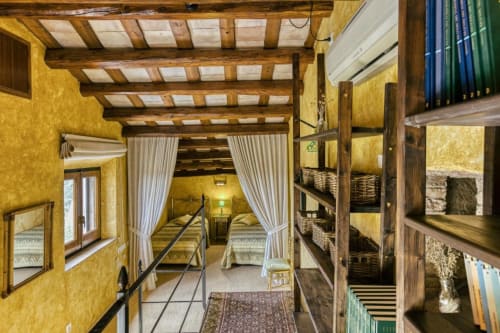 Dormitorio Can Gat Vell en Empordà con vigas de madera, paredes amarillas, cama con dosel y estantería de madera rústica
