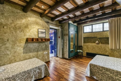 Dormitorio amplio con camas gemelas, vigas vistas, paredes de terracota y vistas al jardín en Can Gat Vell en Gerona