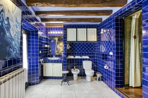 Baño con azulejos azul brillante en Can Gat Vell con doble lavabo, inodoro, bidé, vigas de madera y accesorios blancos en Girona