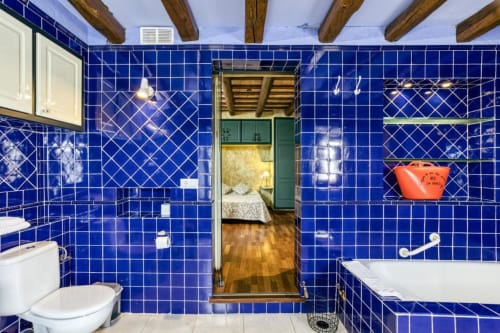 Baño con azulejos azules vibrantes en Can Gat Vell B&B en Girona, con vigas de madera, inodoro blanco y bañera