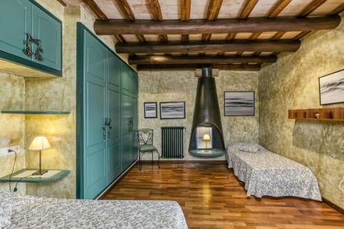 Dormitorio rústico en Can Gat Vell con vigas vistas, armario turquesa y chimenea central.