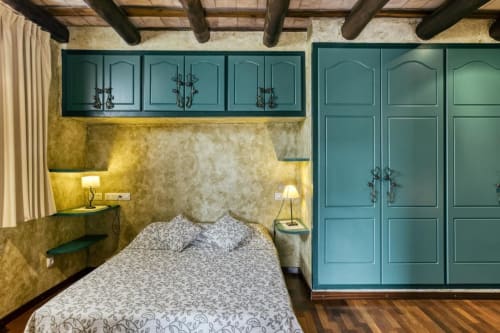 Dormitorio en el B&B Can Gat Vell de Girona con armarios turquesa, paredes mostaza y vigas de madera