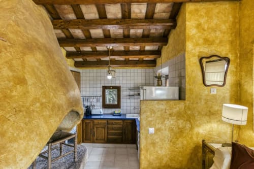 Habitación cálida en tonos amarillos con vigas de madera, salpicadero de azulejos blancos y armarios de madera oscura en Can Gat Vell, Girona