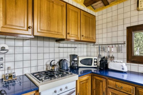 Cocina rústica de la casa rural Can Gat Vell en Girona con gabinetes de madera, encimera azul, estufa de gas y azulejos blancos