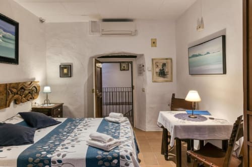 Acogedora habitación en la casa rural Can Gat Vell de Girona con ropa de cama azul estampada, cabecero de madera y zona de comedor con TV.