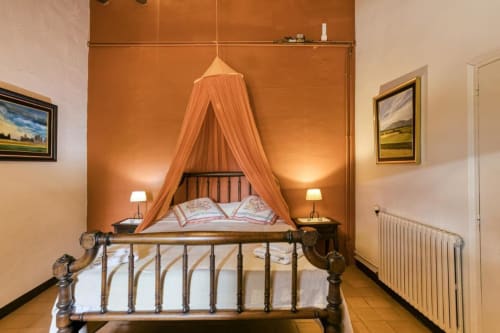 Elegante dormitorio en Can Gat Vell B&B en Girona con cama con dosel, cortinas de tela naranja, marco de madera, lámparas de mesilla y ambiente cálido