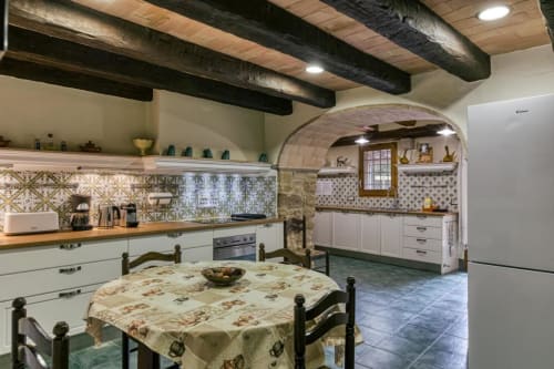 Cocina rústica de la casa rural Can Gat Vell en Girona, Cataluña, con vigas vistas, azulejos decorados y mesa de comedor tradicional.