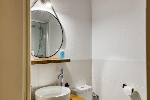 Baño moderno en el Can Gat Vell B&B de Girona con espejo redondo, azulejos blancos y estantería de madera