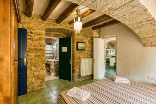 Dormitorio rústico de piedra en Can Gat Vell B&B, Girona, con vigas vistas, ropa de cama a rayas y puertas arqueadas