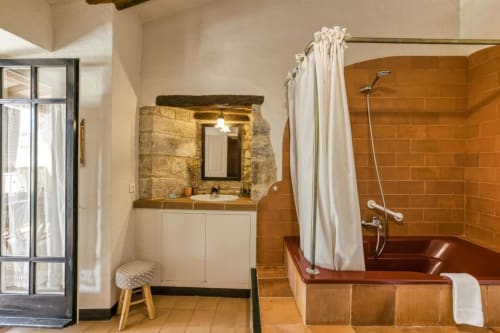 Baño rústico en Can Gat Vell de Girona con baldosas de terracota, lavabo blanco y bañera de madera con cortina de ducha