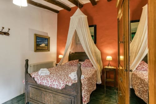 Dormitorio rústico en Can Gat Vell B&B en Girona con cama dosel, ropa de cama roja y paredes de terracota.