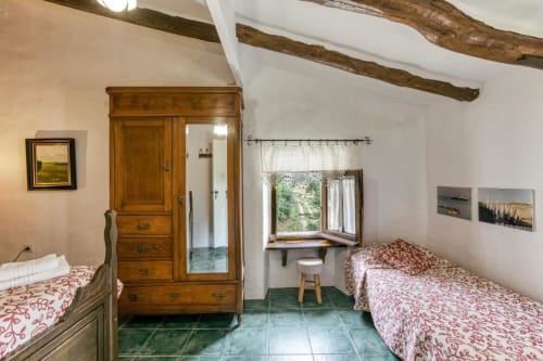 Dormitorio rústico en Can Gat Vell B&B en Girona con camas gemelas, armario de madera, vigas de madera vista y suelo de azulejos verdes