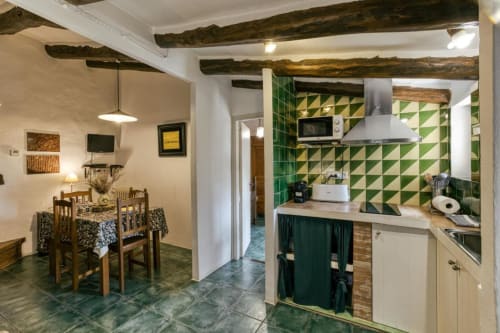 Cocina y comedor del alojamiento Can Gat Vell en Girona con azulejos verdes, vigas de madera y decoración rústica