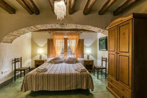 Dormitorio rústico en Can Gat Vell B&B en Girona con vigas de madera, ropa de cama rayada y decoración catalana tradicional