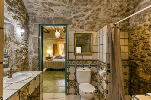 Baño rústico con azulejos decorativos en el Can Gat Vell B&B de Girona, España, con lavabo y ducha de estilo vintage.