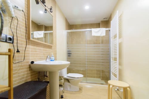 Baño moderno con paredes de azulejos beige, lavamanos pedestal, inodoro y ducha de cristal en el hotel Tradición Rural de Nieva