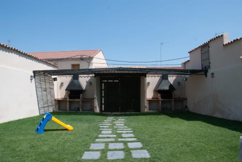 Jardín trasero con césped verde, piedras de paso, tobogán azul y edificios blancos tradicionales del hotel Tradición Rural en Nieva