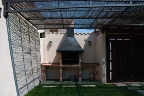 Patio exterior con pérgola, asador de ladrillo y jardín verde en Tradición Rural de Nieva