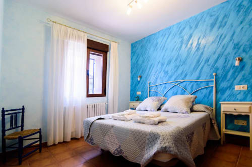 Dormitorio luminoso con paredes azules texturizadas, cama de estructura metálica, ropa de cama crema, suelo de madera y ventana en Tradición Rural de Nieva