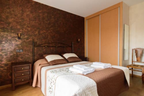 Acogedora habitación en Tradición Rural con paredes texturadas en marrón, cama de hierro forjado y muebles de madera en Nieva